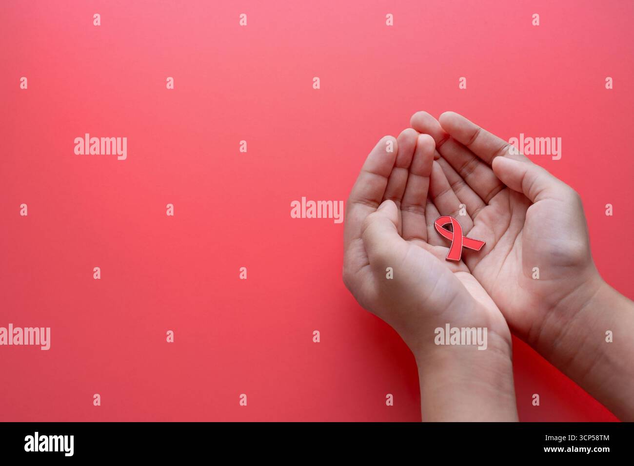 Mani con un nastro rosso di consapevolezza su sfondo rosso. HIV, concetto di sensibilizzazione all'AIDS. Copia spazio per il testo. Foto Stock
