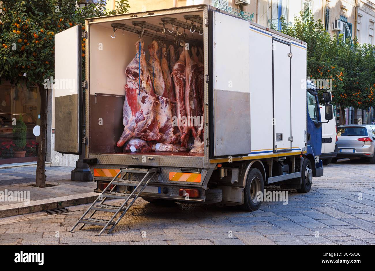 Fabbrica di carne con carne di maiale e manzo appeso ai ganci in un camion di consegna refrigerato. Macelleria magazzino frigorifero per la distribuzione della carne e la catena di approvvigionamento Foto Stock