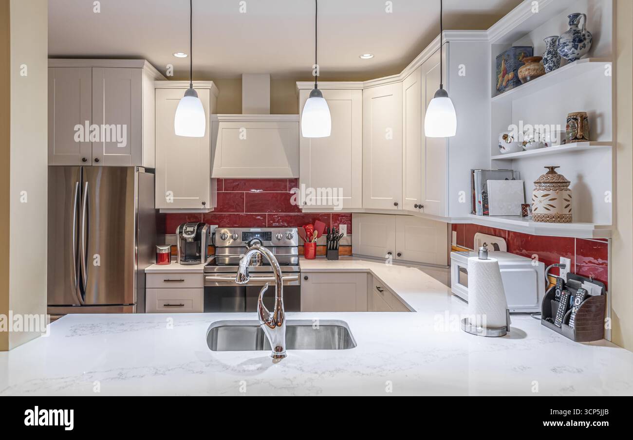 Splendida cucina in una casa di lusso con isola, luci a sospensione e armadi. Moderna cucina interna in agriturismo e lampade luminose. Ripiano in marmo in un mese Foto Stock