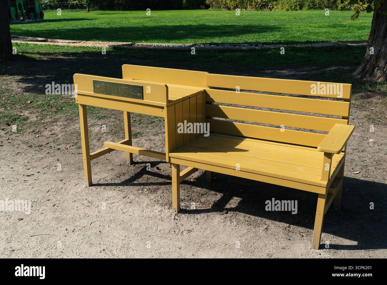 Panca esterna in legno giallo in un parco pubblico, simboleggia lo spazio della comunità, il relax e il design di arredi urbani. Foto Stock