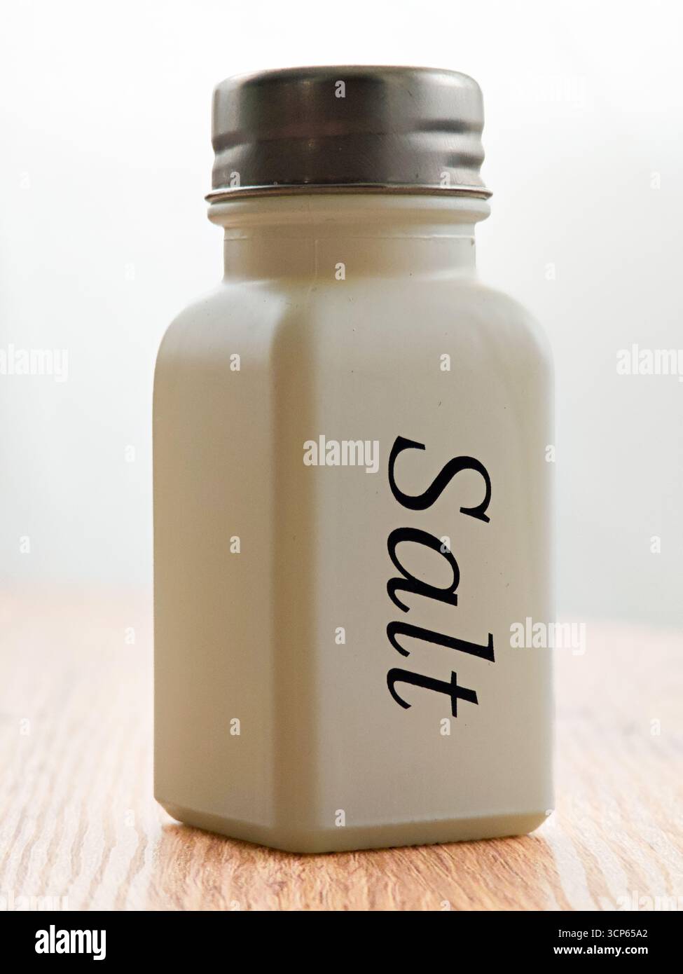 Un agitatore per sale trasparente contiene sale granulato. Presenta un design semplice con la parola Salt stampata sul lato. Questo agitatore è ideale per cucinare tutti i giorni Foto Stock