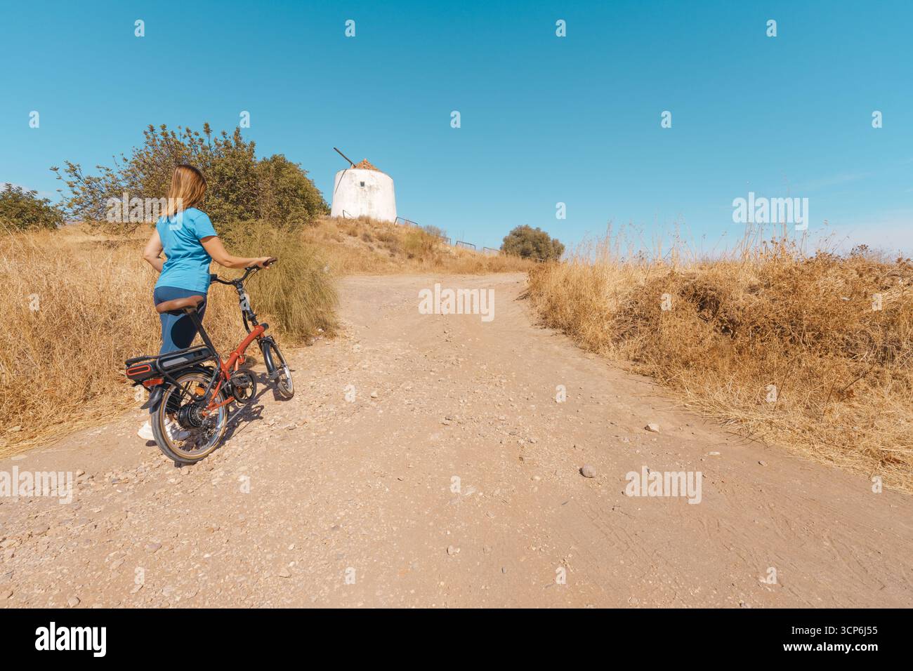 Donna che si avvicina al mulino a vento su un sentiero sterrato Foto Stock