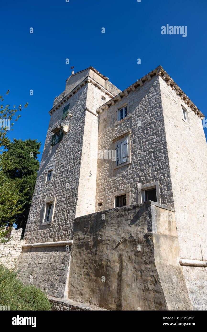La torre di pietra calcarea illuminata dal sole e gli edifici in pietra circostanti formano un cortile storico in una città europea. Le bandiere si aprono sopra, i mattoni e le pietre sono in rilievo Foto Stock