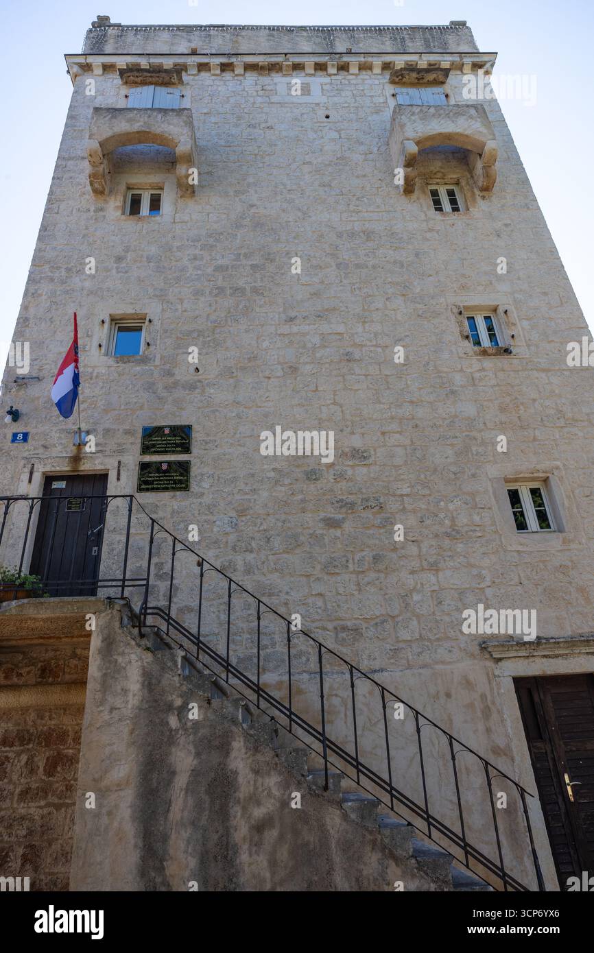 GROHOTE, CROAZIA, 08.23.2025: Un imponente edificio governativo in pietra presenta una bandiera croata, una porta d'ingresso e targhe ufficiali lungo una scala in ferro battuto Foto Stock