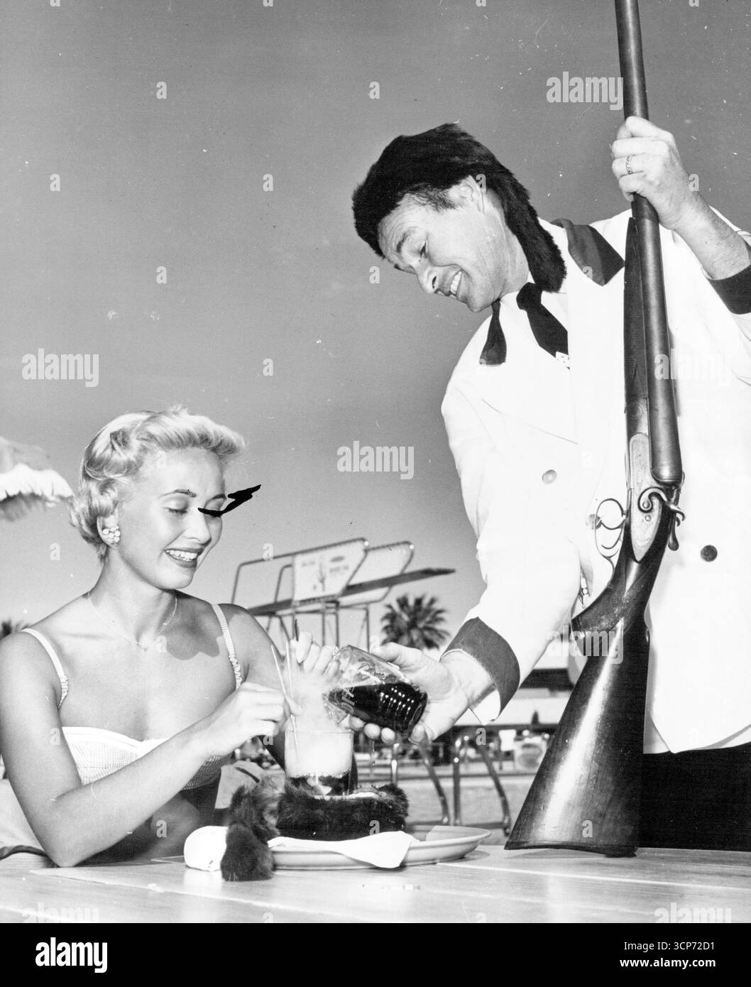 Il ritorno di Davy Crockett - l'UPG adulto non è sfuggito alla mania di Davy Crockett. Qui, un cameriere in un resort di Las Vegas, Nevada, indossa un costume appropriato mentre serve il nuovo cocktail Davy Crockett alla star del cinema Jane Powell. 17 giugno 1955. (Foto di United Press). Foto Stock