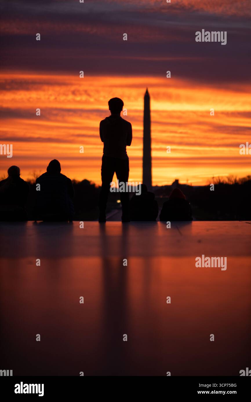 Washington Monument al tramonto con figure sagomate Washington DC // WASHINGTON DC — figure sagomate guardano il tramonto dietro il Washington Monument a Washington DC. Il monumento, un obelisco, è un omaggio a George Washington, il primo presidente degli Stati Uniti. Completata nel 1884, è la struttura in pietra più alta del mondo e la struttura in pietra più alta della Terra. Il monumento si erge come punto focale del National Mall ed è un punto di riferimento significativo nella capitale. Foto Stock