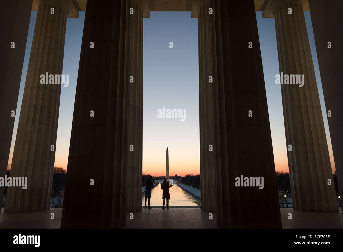 Lincoln Memorial Washington DC con Washington Monument View // WASHINGTON DC - il Lincoln Memorial, un monumento neoclassico dedicato al 16° presidente degli Stati Uniti Abraham Lincoln, è visto attraverso le sue colonne torreggianti, incorniciando una vista lontana del Washington Monument. Il memoriale è situato all'estremità occidentale del National Mall ed è un punto di riferimento significativo nella capitale. Completato nel 1922, è costruito in marmo e include una grande statua seduta di Lincoln. Il design del monumento trae ispirazione dagli antichi templi dorici greci. Foto Stock