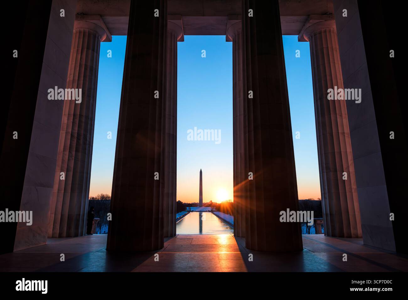 Lincoln Memorial Columns con Washington Monument Washington DC // WASHINGTON DC - il colonnato del Lincoln Memorial incornicia una vista del Washington Monument e della piscina riflettente durante l'alba. Completato nel 1922, il Lincoln Memorial onora il sedicesimo presidente degli Stati Uniti, Abraham Lincoln, ed è un importante punto di riferimento sul National Mall. Il Washington Monument, un obelisco che commemora George Washington, è la struttura più alta di Washington D.C. e una caratteristica centrale del nucleo monumentale della città. Il design del monumento, ispirato ai templi dorici greci, presenta 36 colonne che rappresentano il 36 ° Foto Stock