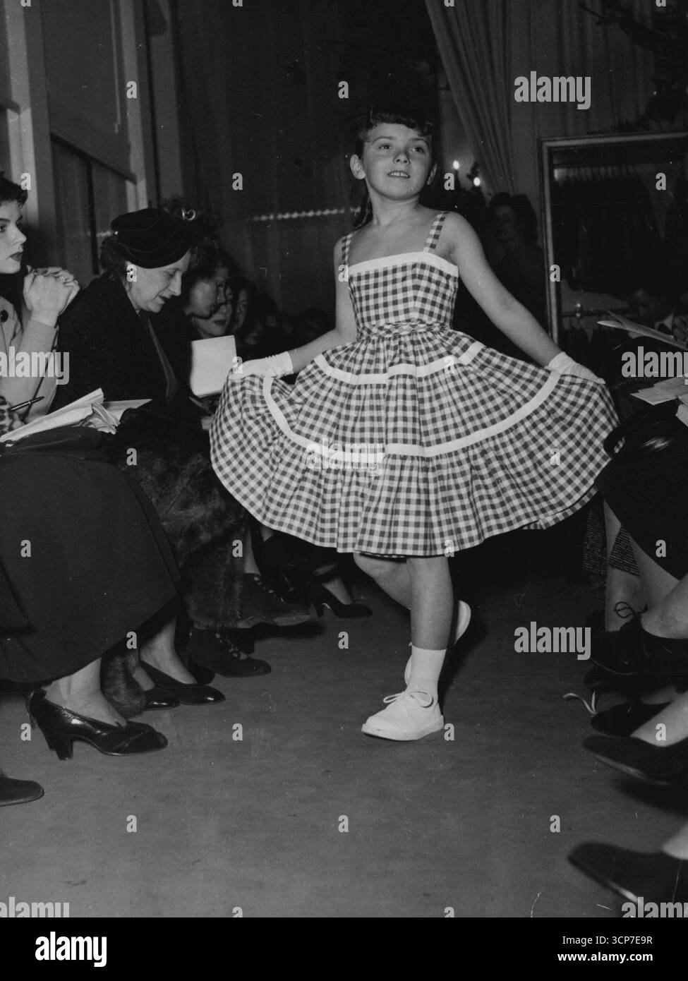 Pomme, 10 anni, posa in un prendisole in lino a quadri rosso e bianco con una gonna a balze, spalline, finiture bianche. Con questo, guanti corti. 24 aprile 1952. (Foto di Intercontinentale). Foto Stock