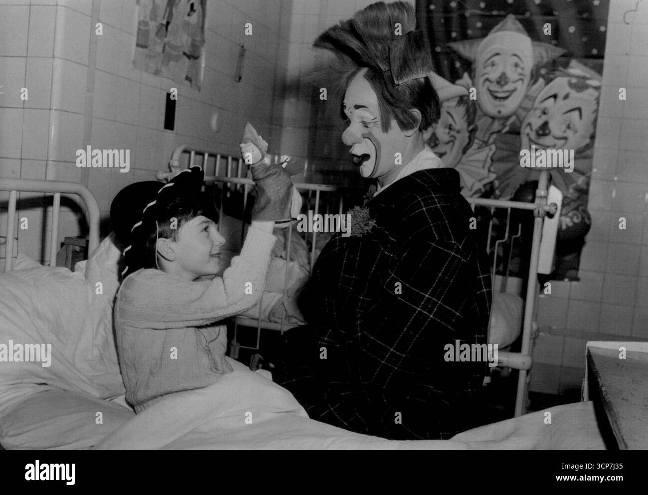 Bedside LaughsLondon: Il bambino di otto anni Peter Coulter, di Hampstead, mostra il suo burattino a Coco Jnr., uno dei clown del circo di corte di Jack Hylton, che ancora oggi intratteneva bambini malati all'Elizabeth Garrett Anderson Hospital di Euston Road, Londra. 29 dicembre 1952. Foto Stock
