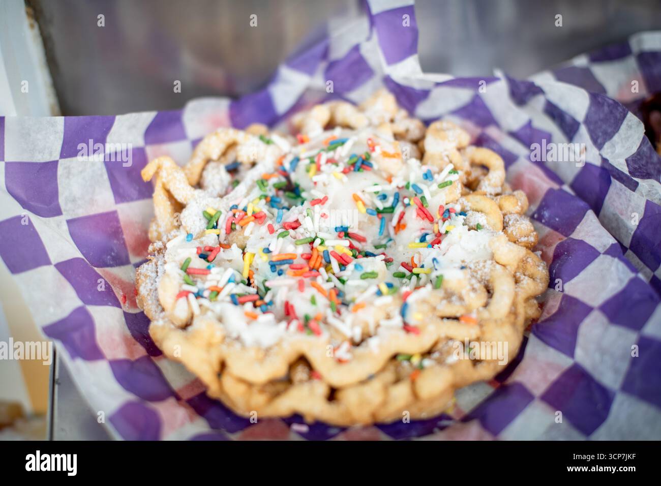 Torta a imbuto con Sprinkles Frederick Fairgrounds Frederick Maryland // FREDERICK, Maryland — Una torta a imbuto, una pasta fritta spolverata con zucchero a velo e ricoperta di glassa bianca e arcobaleno, viene presentata in un involucro di carta a scacchi alla Great Frederick Fair. La zona fieristica si trova a Frederick, Maryland, Stati Uniti. Foto Stock