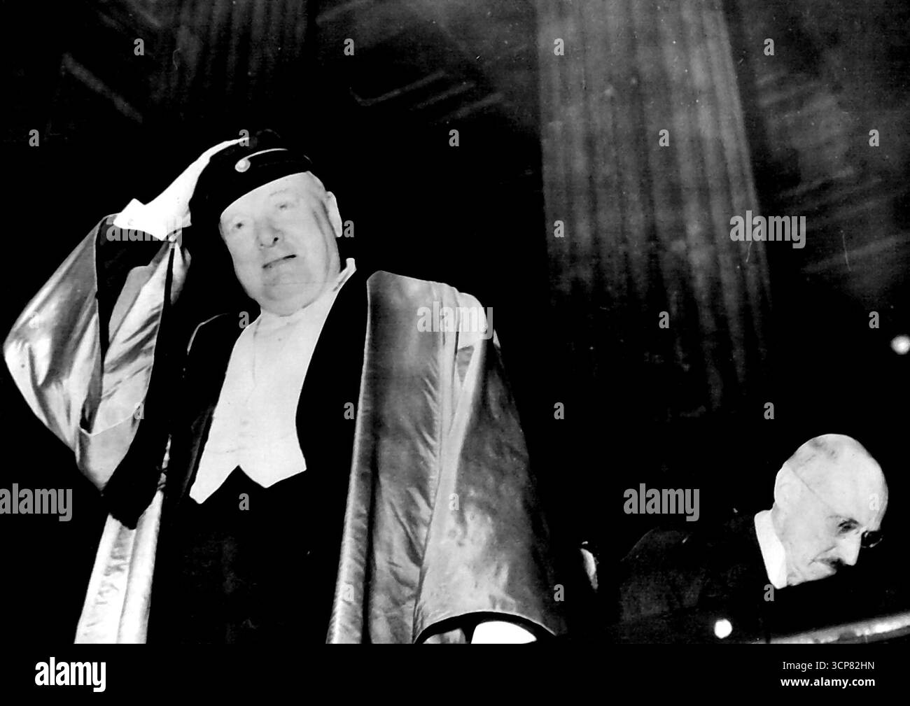Churchill Honoured - Gets New Hat -- Mr. Winston Churchill, tiene il suo nuovo berretto di seta nera quando lascia l'Università di Oslo dopo che gli è stata conferita la laurea honoris causa di dottore in filosofia, durante la sua visita in Norvegia. Il tappo, al quale è attaccata una lunga nappina, è l'equivalente di Olso del mortaio (per gli Acadamicians e gli studenti). Appoggiandosi in avanti in auto (a destra) un re Haakon che ha anche partecipato alla cerimonia. 14 maggio 1948. Foto Stock