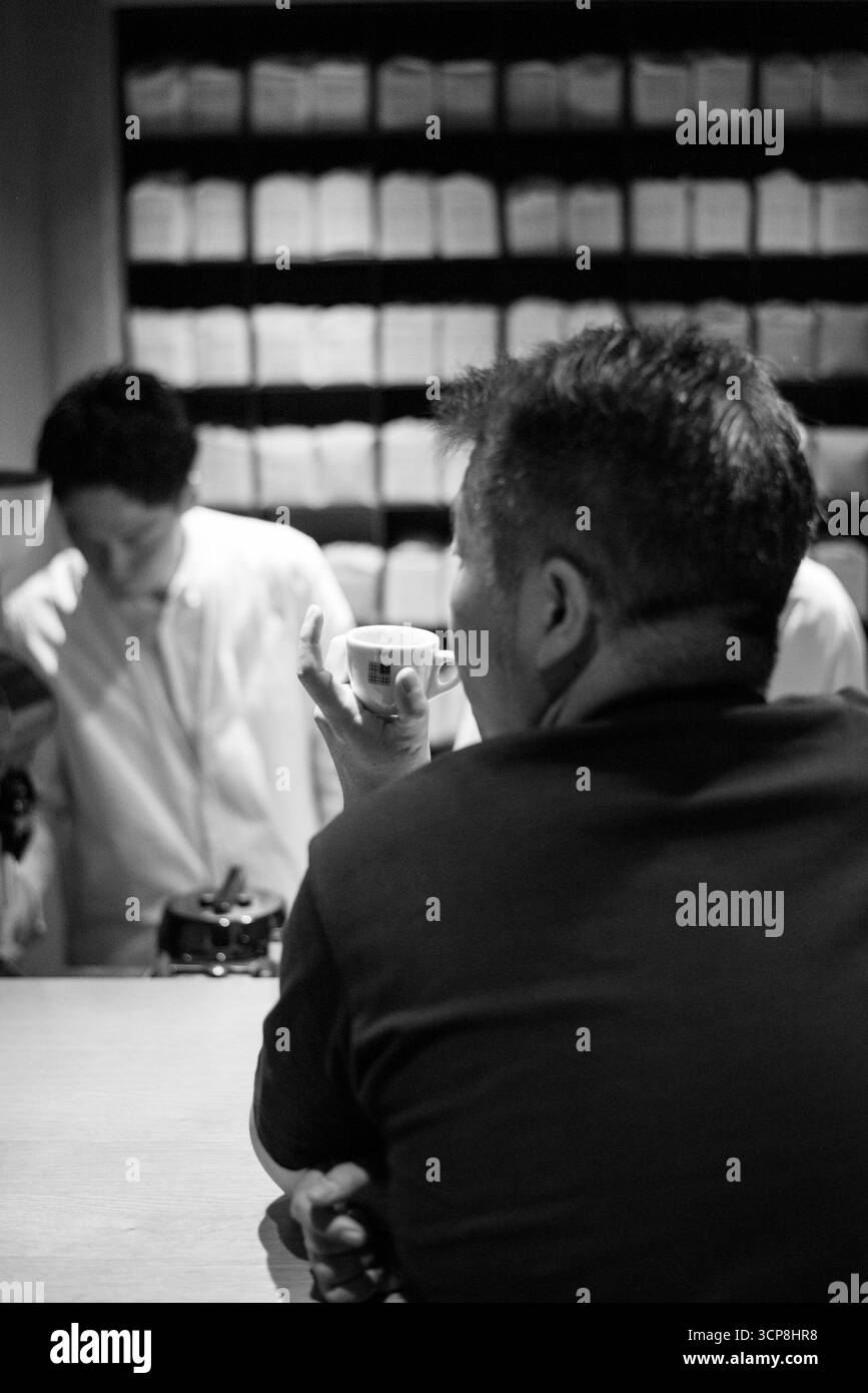 TOKYO, GIAPPONE- 27 OTTOBRE 2024: TOKYO, GIAPPONE- 27 OTTOBRE 2024: Foto in bianco e nero di un uomo giapponese che tiene una tazza di caffè al KOFFEE MAMEYA, A. Foto Stock