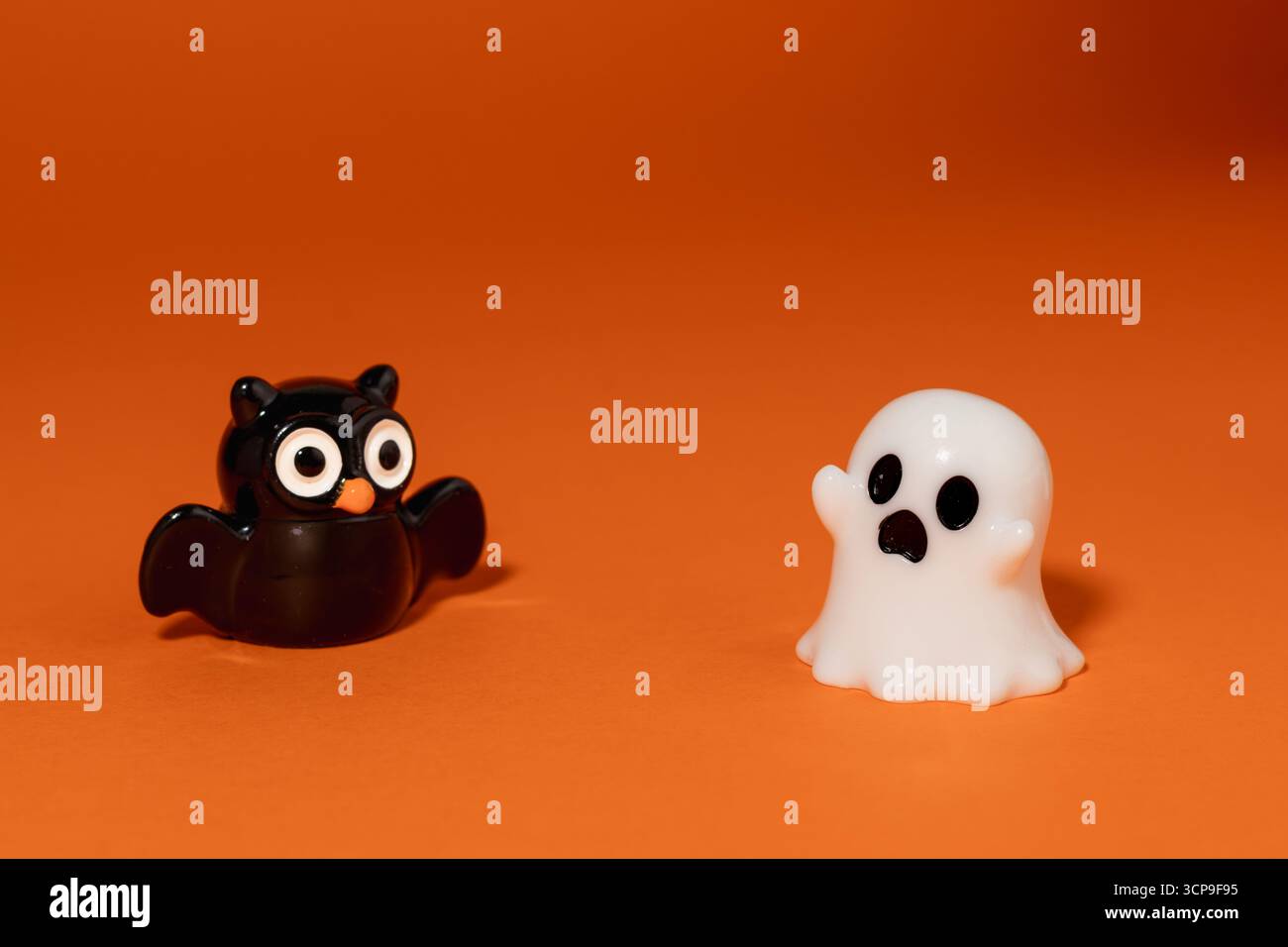 Divertente scena di Halloween con una piccola statuetta fantasma che fa paura di un gufo nero su uno sfondo arancione. Foto Stock