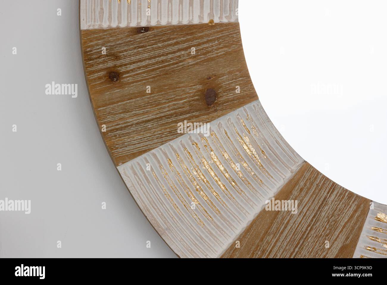 Primo piano di una cornice a specchio decorativa circolare con pannelli in legno alternati e sezioni testurizzate bianche con dettagli in lamina dorata. Perfetto per mod Foto Stock