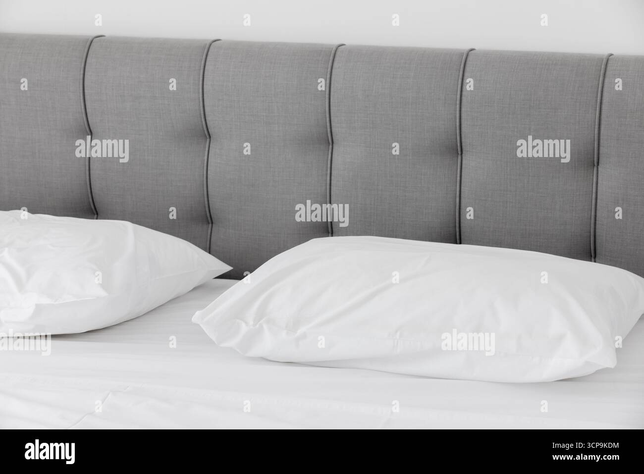 Un letto ben fatto presenta una soffice testata grigia e cuscini bianchi, creando una tranquilla e minimalista camera da letto adatta per l'arredamento della casa, gli hotel e la vita Foto Stock