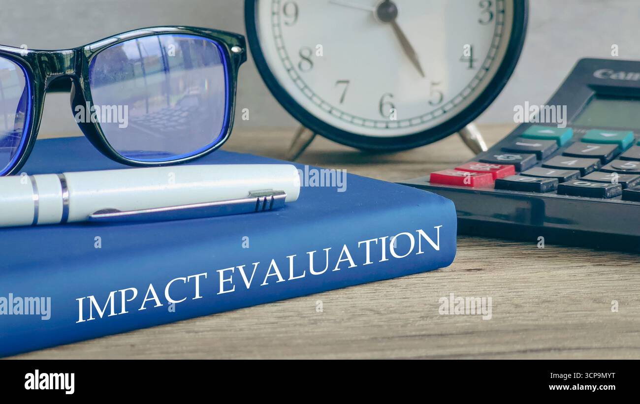 Occhiali, orologio e calcolatrice su un libro intitolato "VALUTAZIONE D'IMPATTO", che rappresenta l'analisi aziendale. Foto Stock