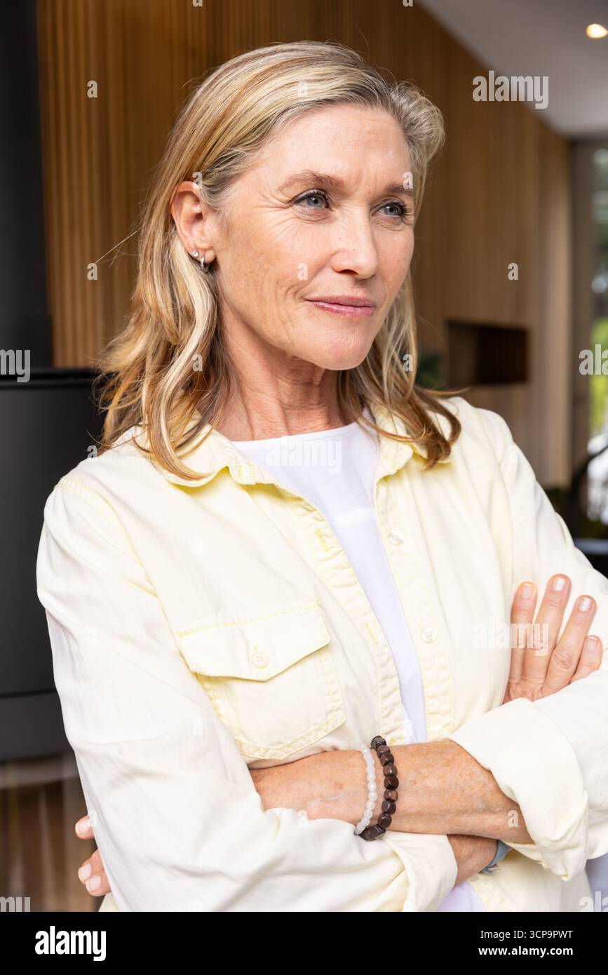 Donna anziana in piedi con le braccia piegate nel soggiorno da una stufa cilindrica nera Foto Stock