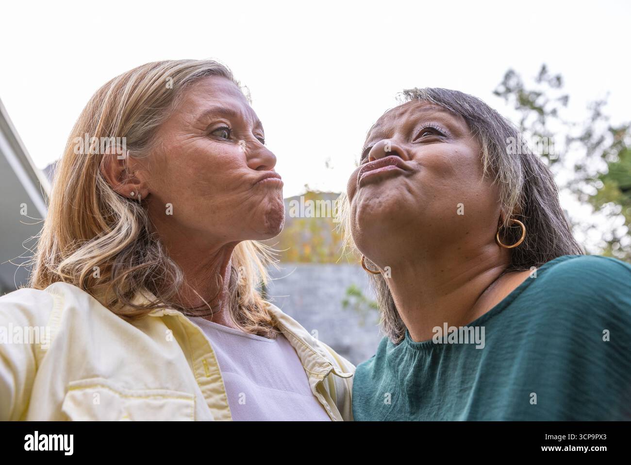 Diverse amiche femminili che fanno espressioni fish-face mentre si appoggiano a vicenda nel cortile Foto Stock