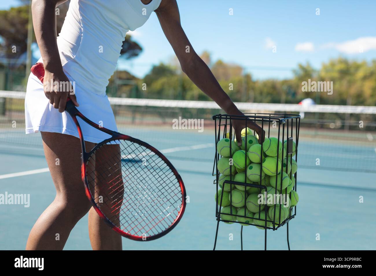 Tennista donna afroamericana che raccoglie palle dal cestino sul campo blu, copia spazio Foto Stock