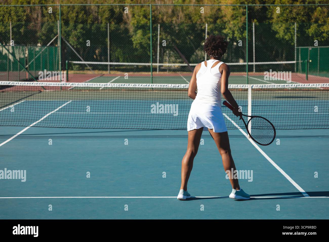 Tennista afroamericana adulta in piedi su un campo duro a una racchetta di tenuta Foto Stock