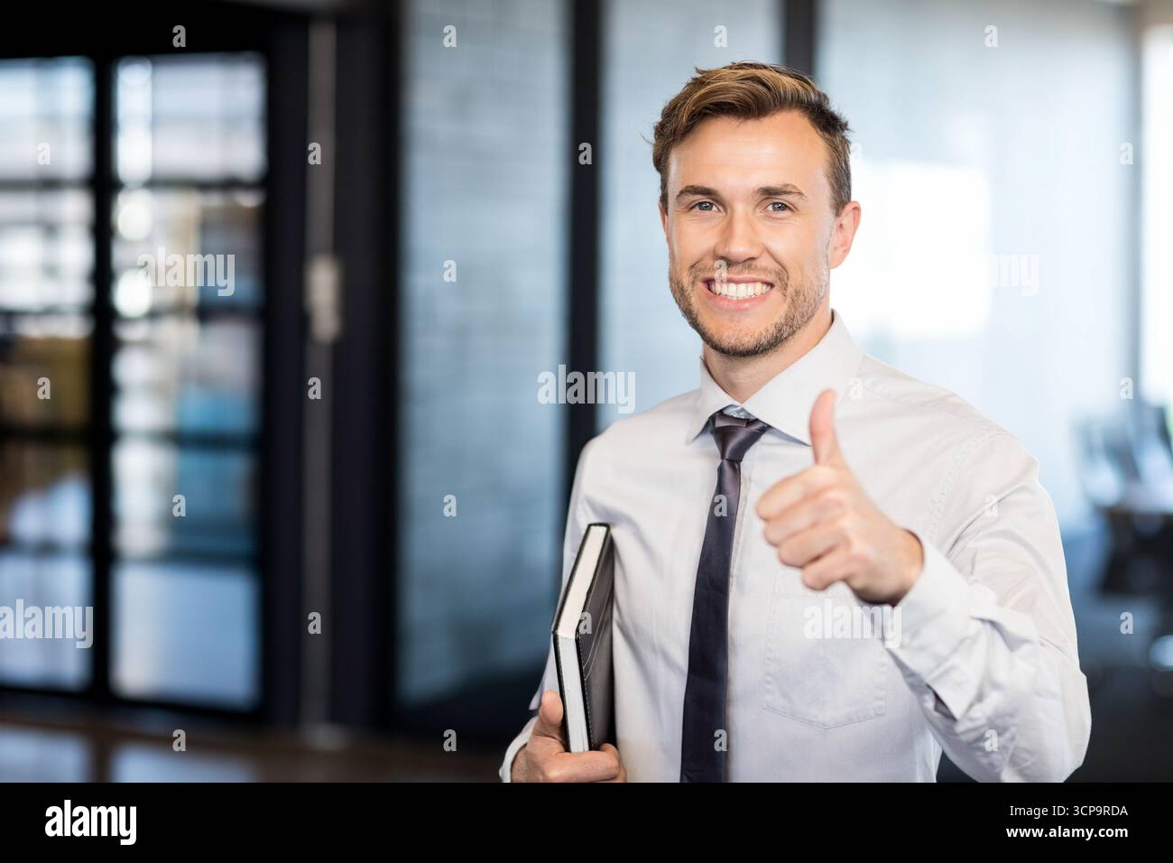 Professionisti aziendali in piedi in ufficio con pannelli di vetro che contengono due notebook con pollice in alto Foto Stock