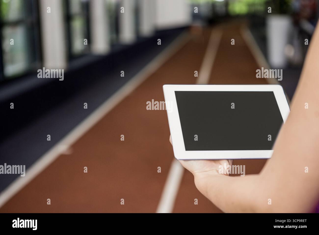 Adulto che tiene un tablet e studia corsie all'interno del palazzetto dello sport con filtraggio alla luce del sole Foto Stock