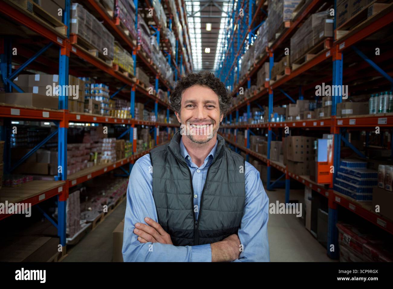 I rack blu e arancioni si trovano nella corsia del magazzino, mentre tengono le scatole di cartone sotto luci accese Foto Stock