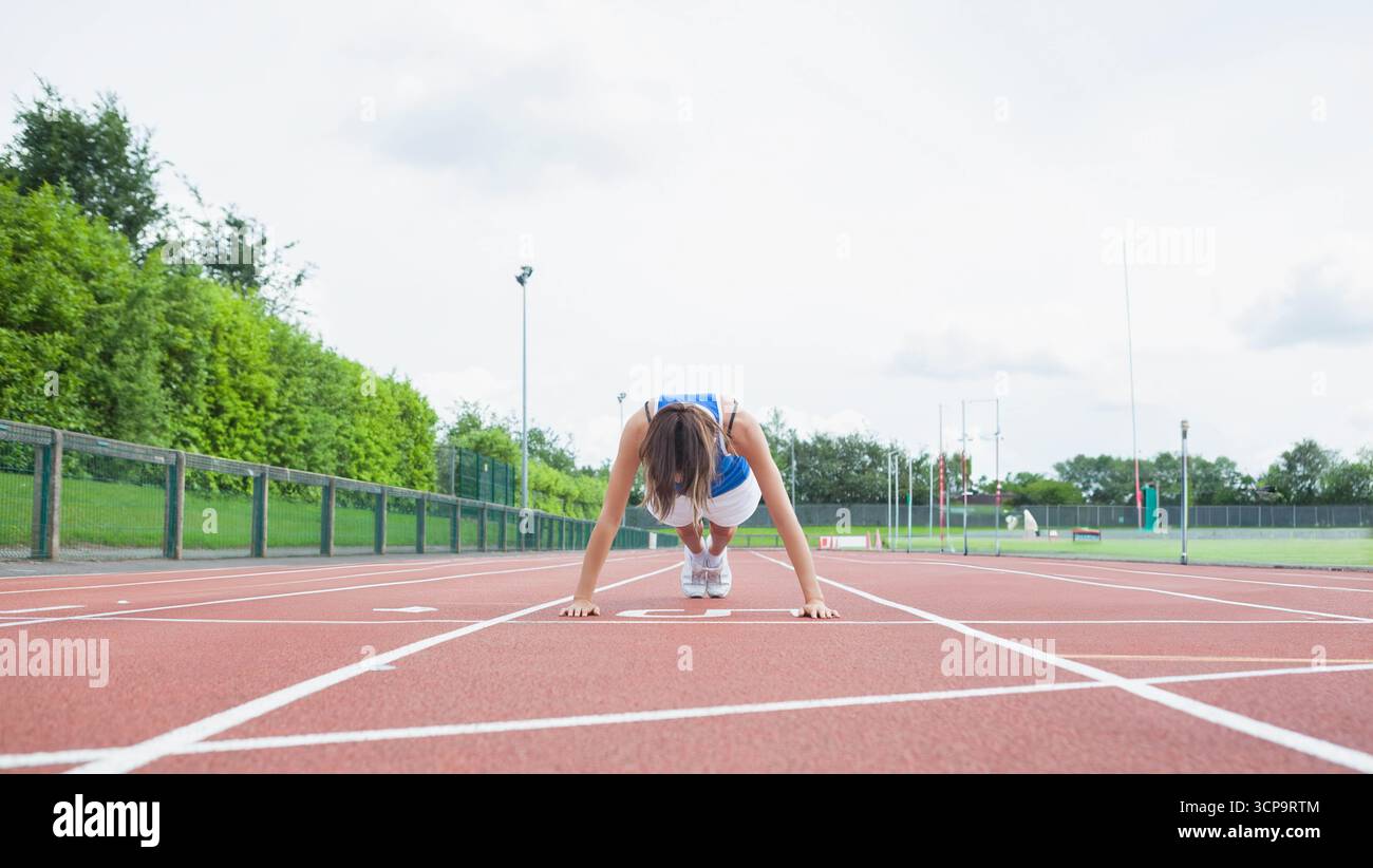 Donna accovacciata con le mani sulla linea di partenza bianca su pista rossa che indossa scarpe da running bianche Foto Stock