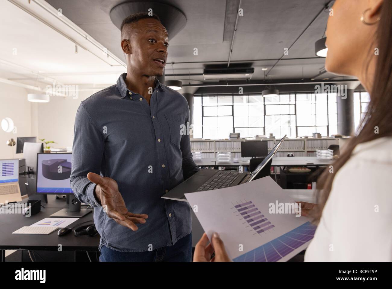 Colleghi diversi che analizzano i dati dei grafici a barre con un laptop, grafici in un ufficio open space Foto Stock