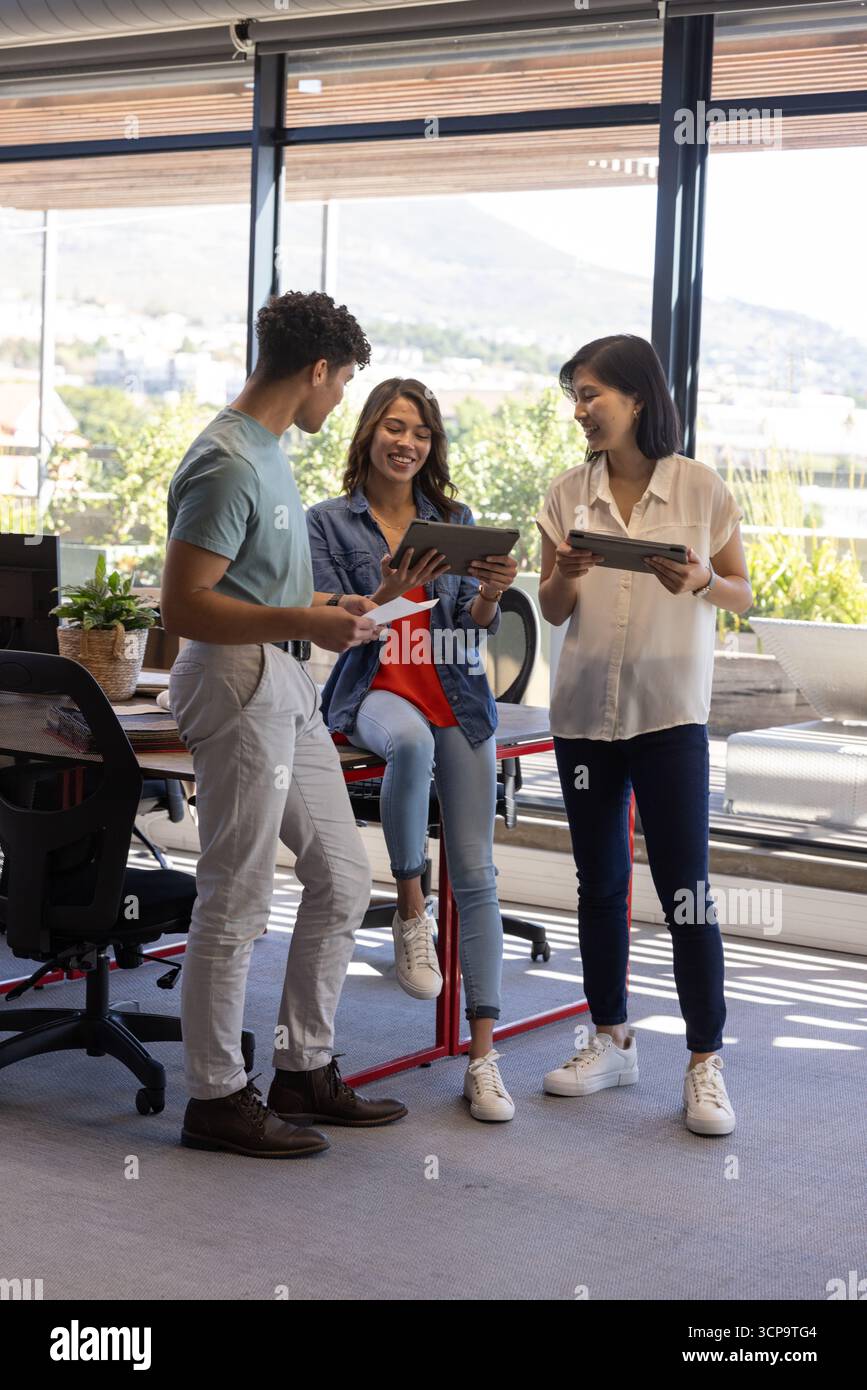 Diversi colleghi che collaborano intorno alla scrivania in piedi in un ufficio moderno con tablet Foto Stock