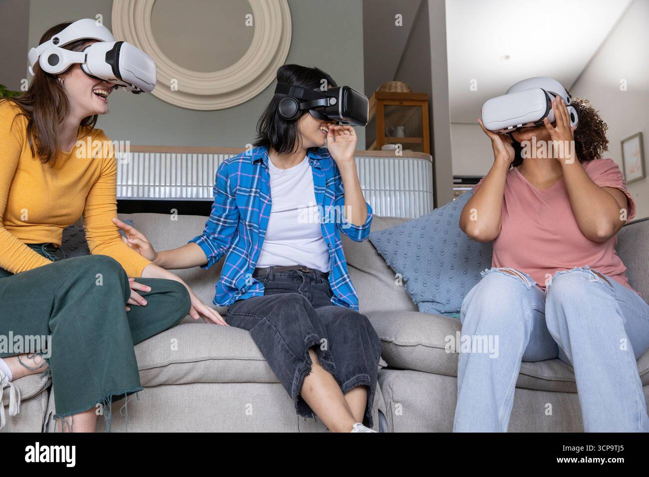 Diverse amiche che indossano occhiali VR e si siedono sul divano grigio in salotto Foto Stock