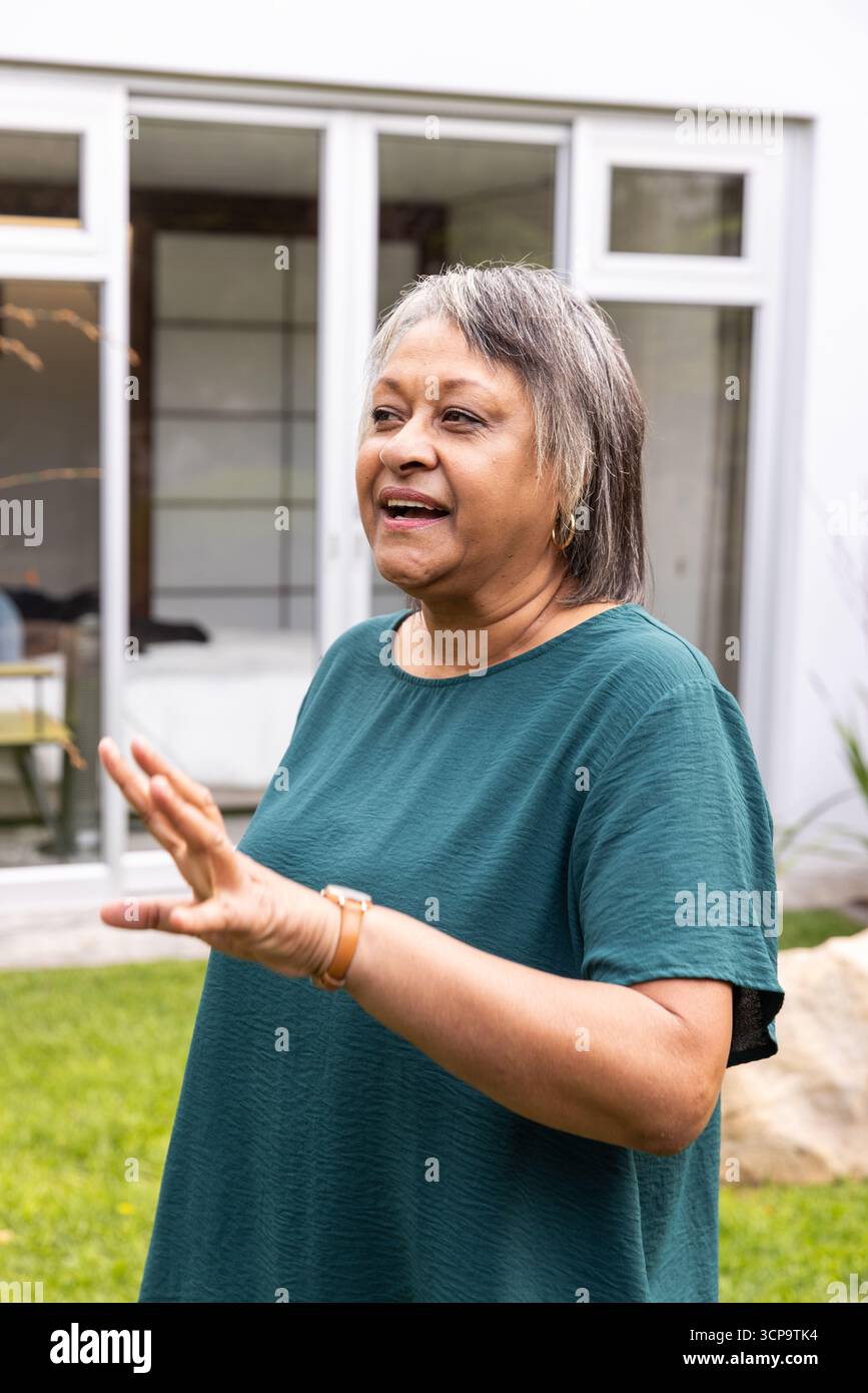 Donna afroamericana anziana in piedi sul prato davanti a porte di vetro che parla mentre gestiva Foto Stock