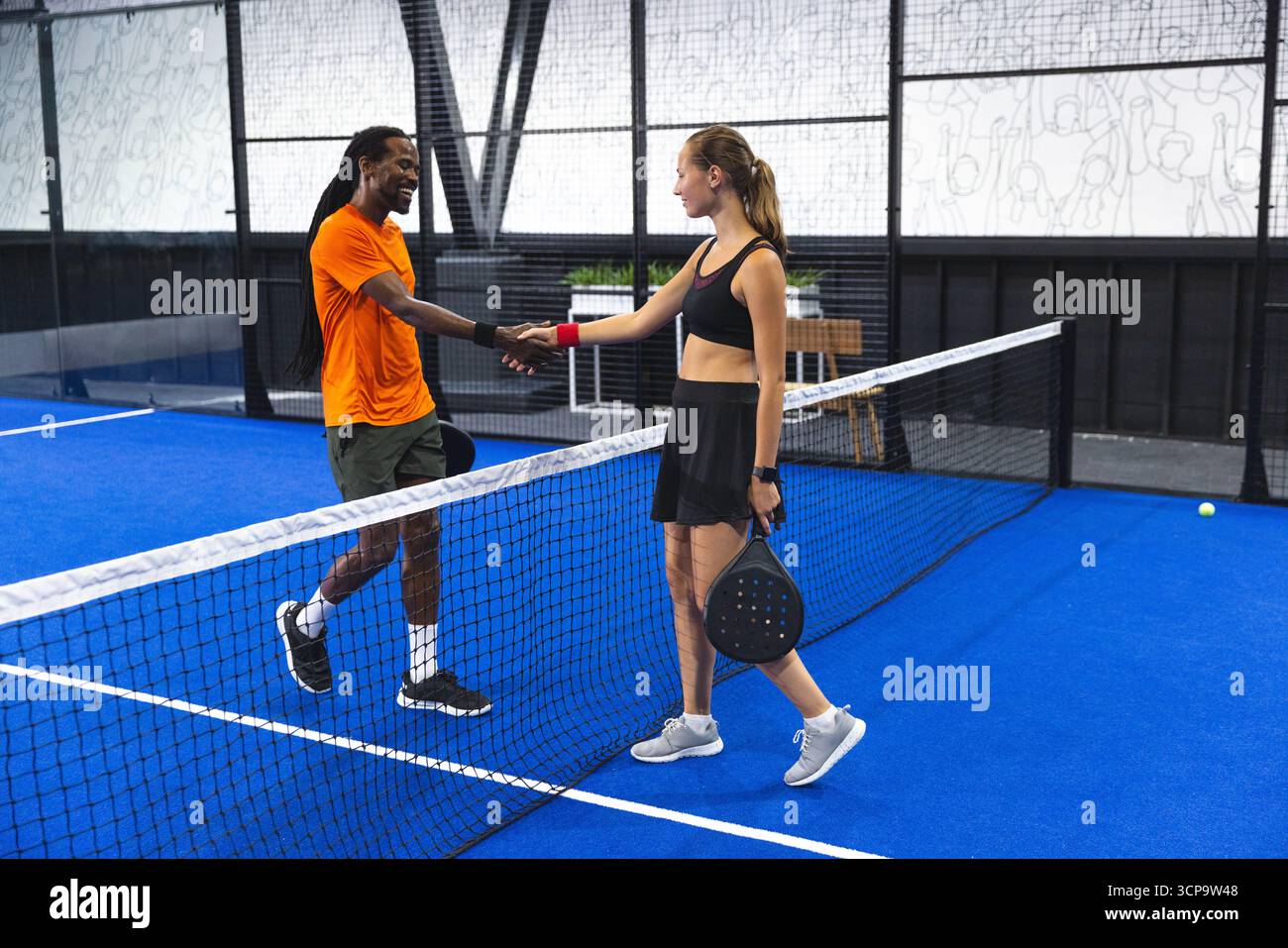 Diversi giocatori indossano abbigliamento sportivo che stringono le mani sulla rete sul campo del padel con le pagaie e la palla gialla Foto Stock
