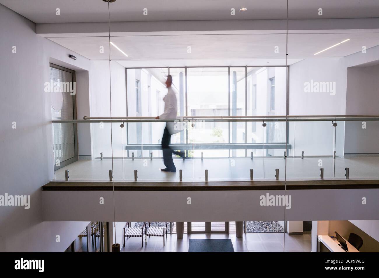 Passerella rivestita in vetro che si estende sul corridoio superiore e si affaccia sulla hall sottostante, con luce a sospensione sopra Foto Stock