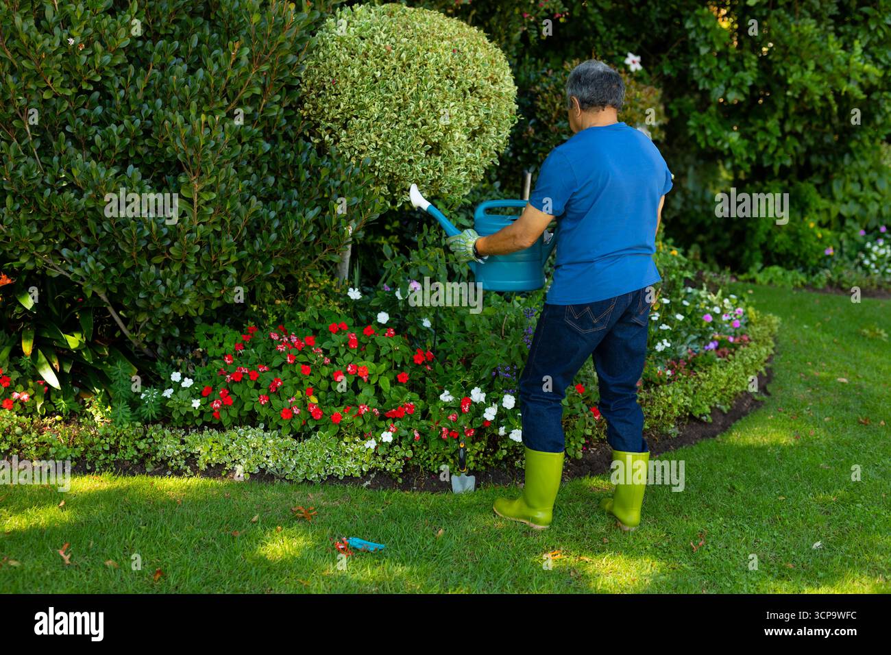 Uomo anziano che innaffia piante nel giardino del cortile con barattolo di plastica verde e cazzuola, spazio copia Foto Stock