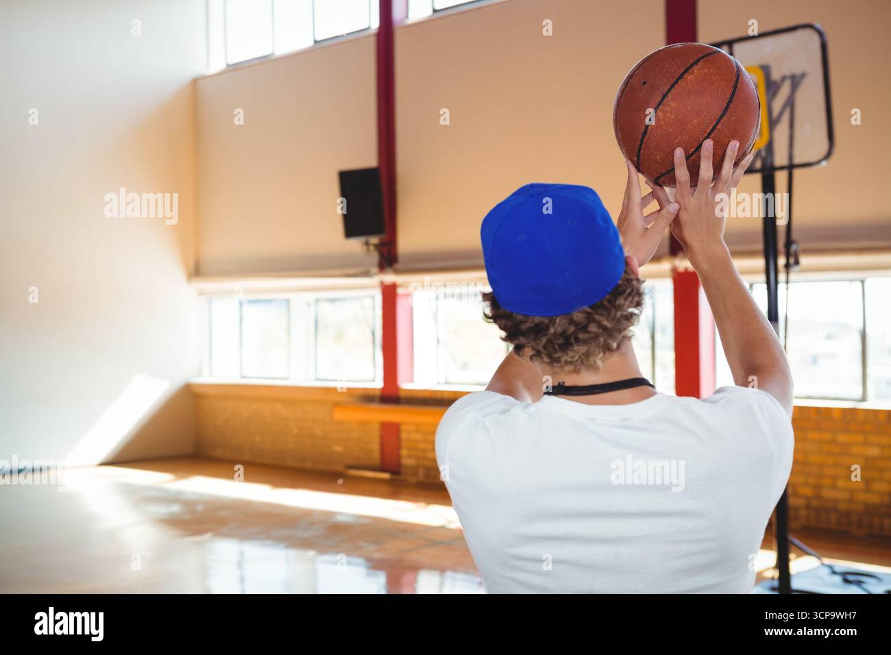 Ragazzo che tiene il pallacanestro sopra la testa e prepara i colpi sul campo da palestra con il cerchio portatile Foto Stock