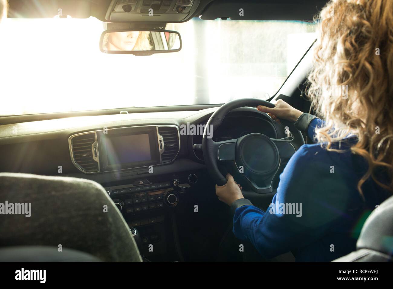 Donna di medie dimensioni che indossa una giacca blu scuro che tiene il volante all'interno dell'auto e lancia la luce parassita della lente Foto Stock