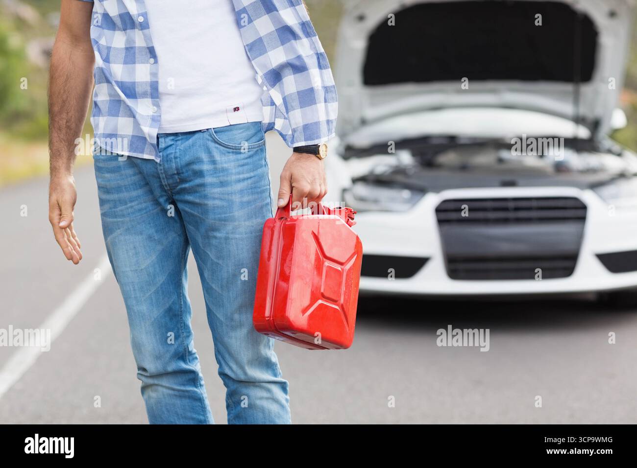 Maschio adulto medio che tiene il serbatoio del carburante rosso accanto alla berlina bianca con cappuccio aperto sulla strada rurale Foto Stock