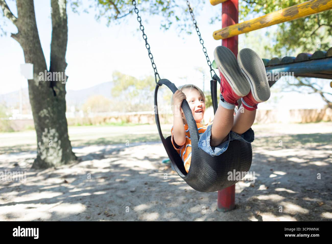 Ragazzo che si appoggia sul sedile altalena appeso alle catene sul palo rosso nel parco giochi, spazio per copiare Foto Stock