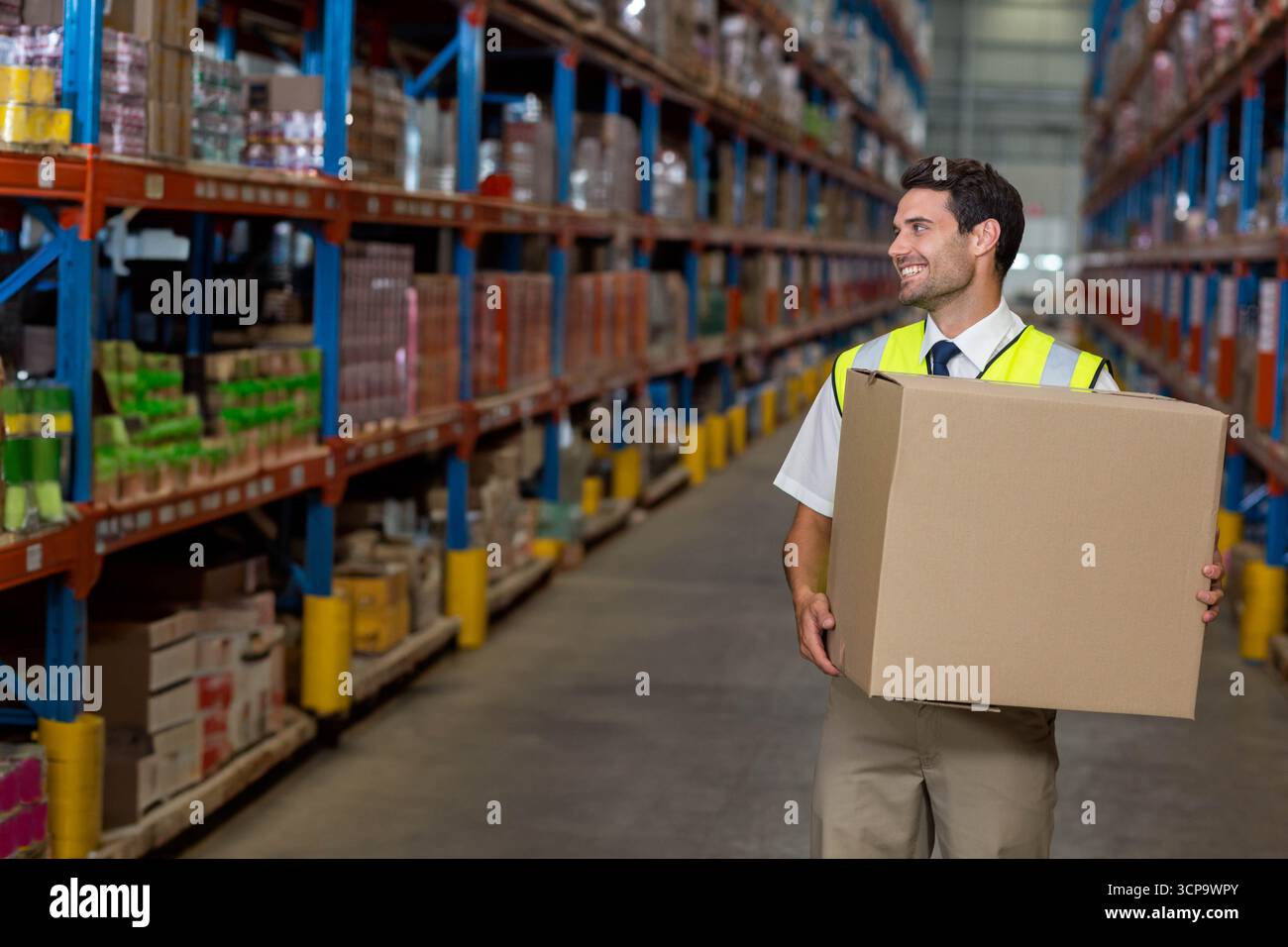 Pile di scatole di cartone che si estendono su alti rack metallici lungo il corridoio del magazzino sotto luci accese Foto Stock