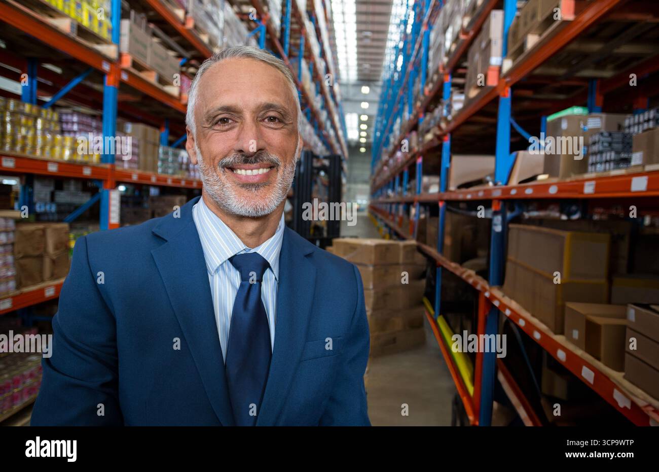 Scaffali che si innalzano in magazzino, tenendo scatole di cartone pallettizzate lungo la lunga corsia centrale sotto le luci Foto Stock