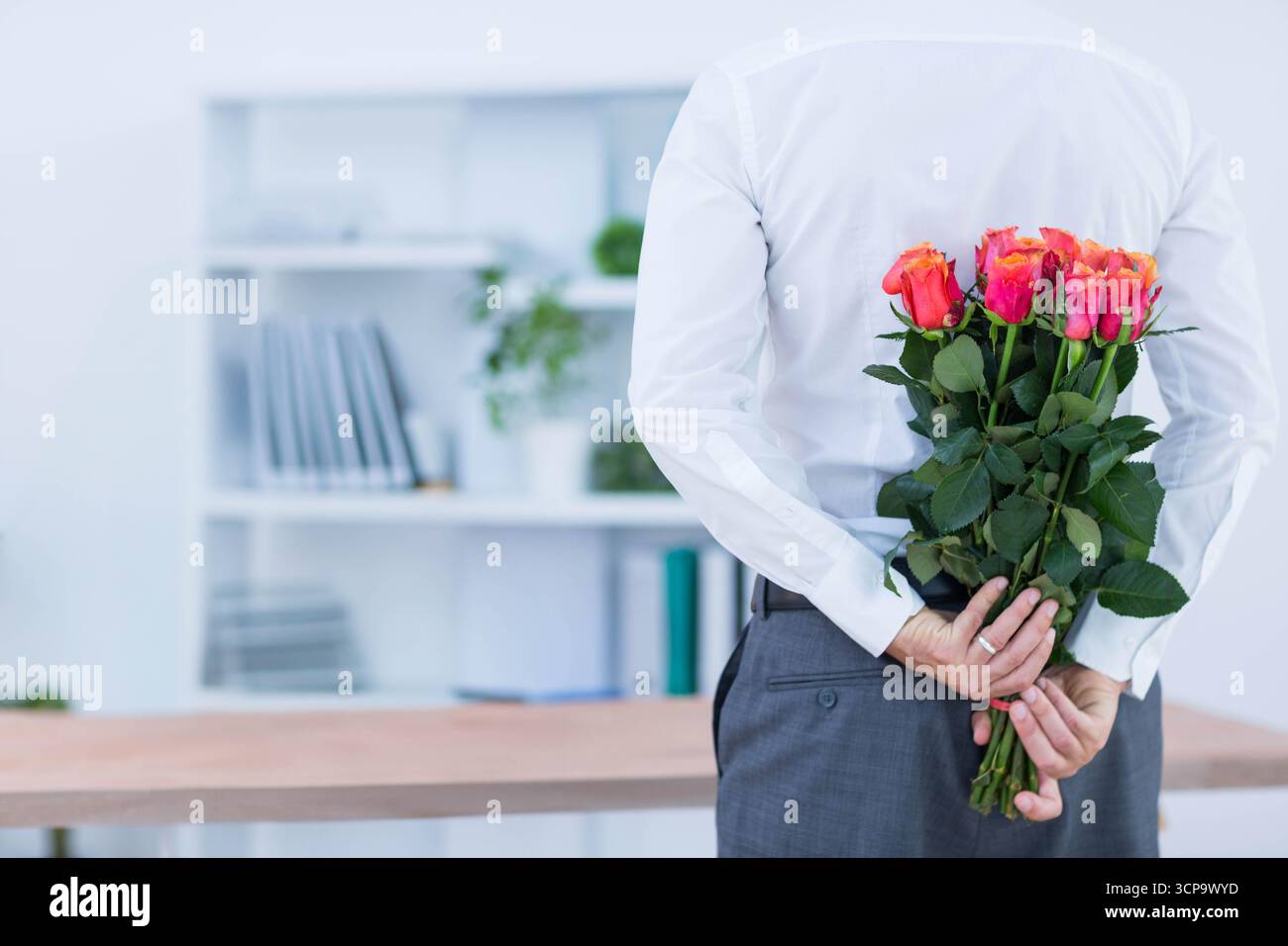 Uomo maturo in carica con bouquet di rose rosa-arancio dietro la scrivania, spazio per fotocopie Foto Stock