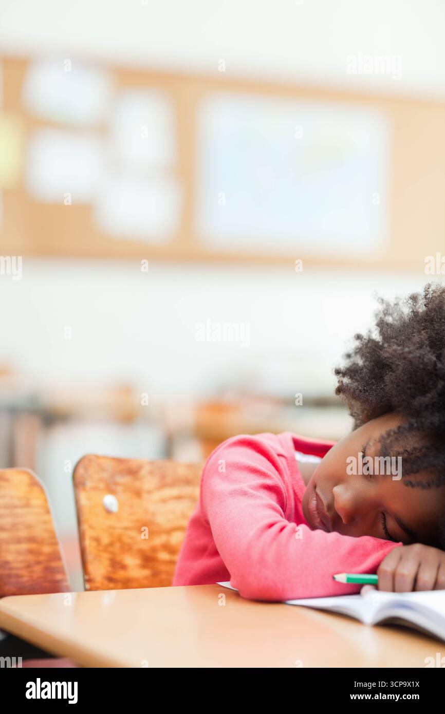 Ragazza afroamericana che riposa la testa su un libro con matita alla scrivania in classe, spazio fotocopie Foto Stock