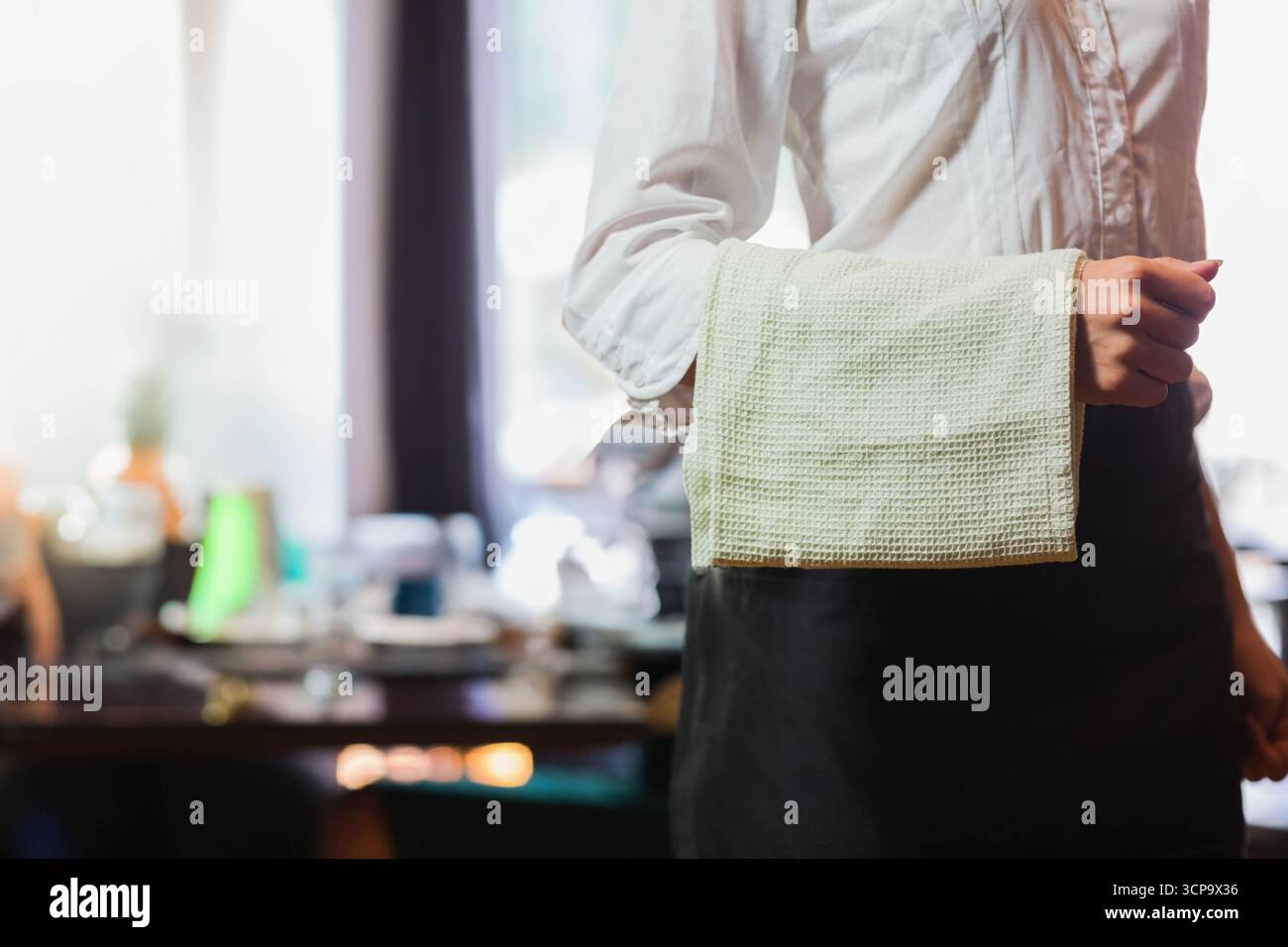 Asciugamano in tessuto di cialde che avvolge il grembiule in vita nero nella sala da pranzo del ristorante, con tavoli fissi Foto Stock