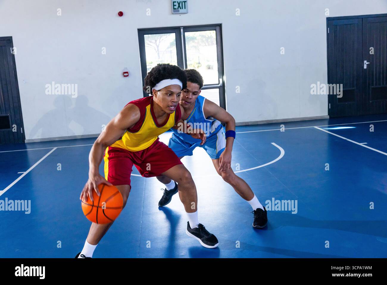 Atleti afroamericani maschili che dribblano mentre sono sorvegliati sul campo con palla arancione e cartello di uscita Foto Stock