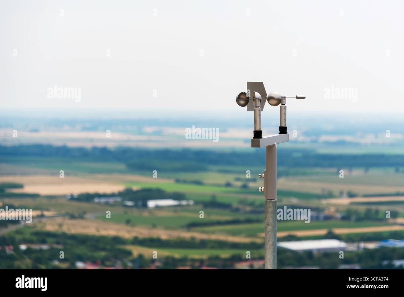Primo piano di un anemometro utilizzato per misurare la velocità del vento, posizionato su una collina con campi sfocati e cielo sullo sfondo Foto Stock