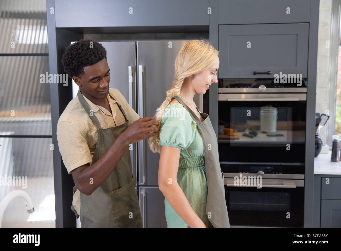 Diverse coppie che legano le cinghie del grembiule in una cucina moderna con forno doppio e frigorifero Foto Stock