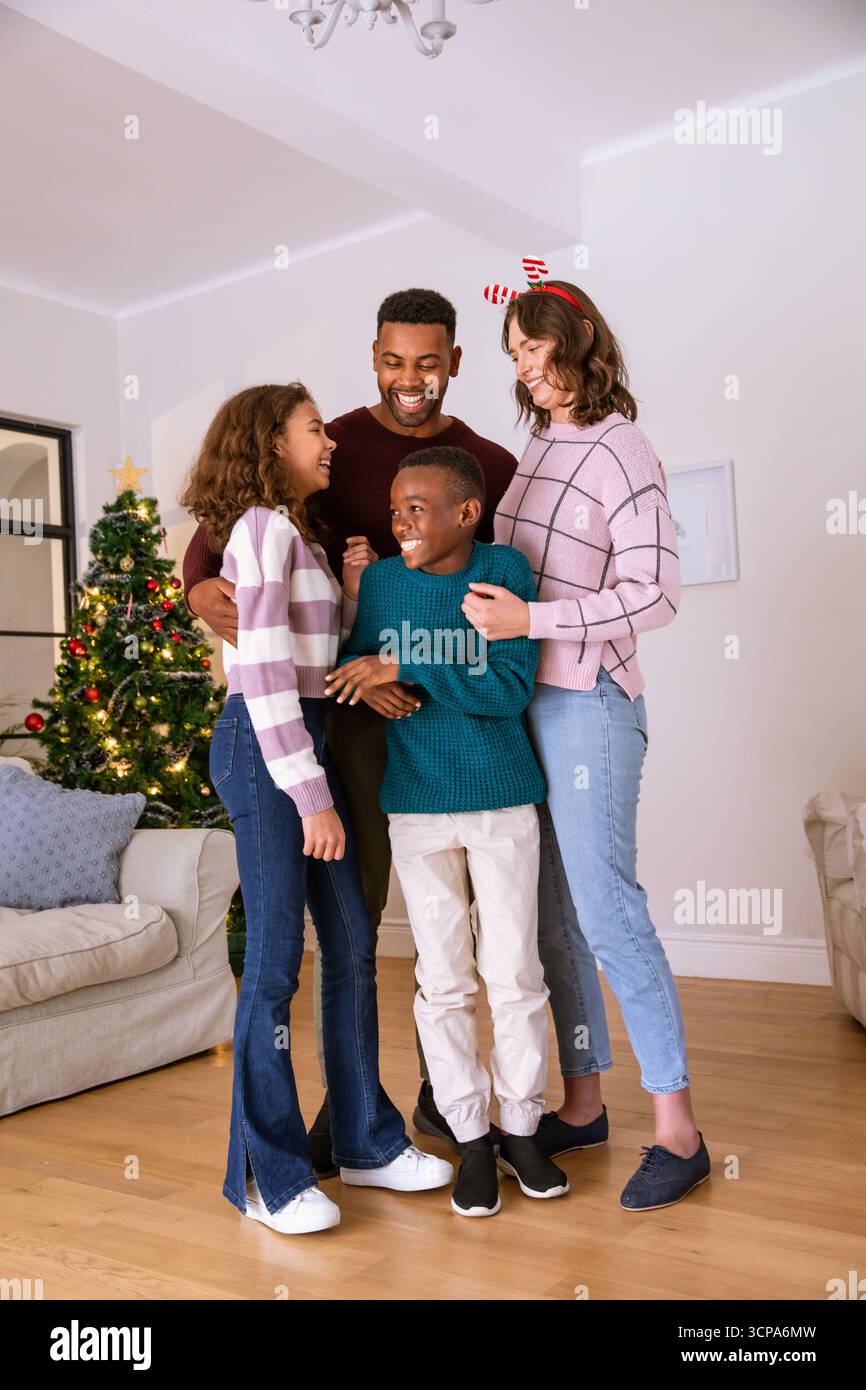 Famiglie diverse che abbracciano e sorridono nel soggiorno vicino all'albero di natale decorato e al lampadario Foto Stock
