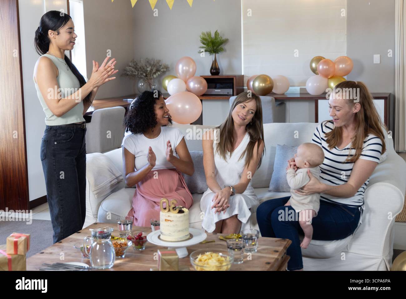 Diverse amiche sedute sul divano in soggiorno per festeggiare, palloncini e neonati Foto Stock